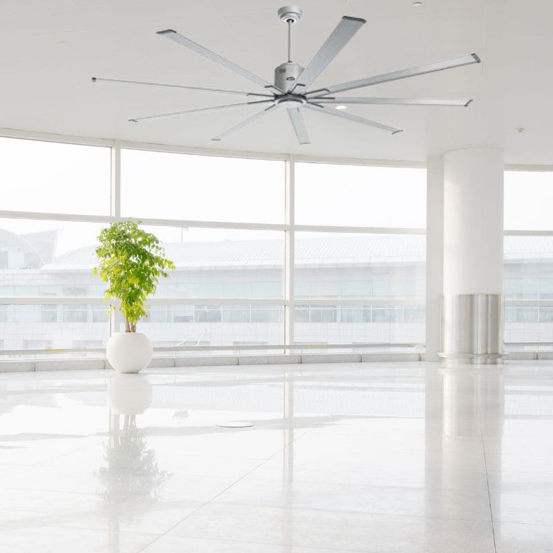 Ventilateur mural industriel dans un hall lumineux avec plante en pot, décor minimaliste et sols miroitants. déstratificateur d air industriel recherché ici.
